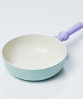 A pastel-colored wok with a light green body and a purple handle, displayed on a white background