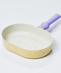 A pastel-colored grill pan with a yellow body and a purple handle, displayed on a white background