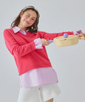 A woman in a cream sweatshirt holding a yellow frying pan with a purple handle, smiling and posing against a purple background