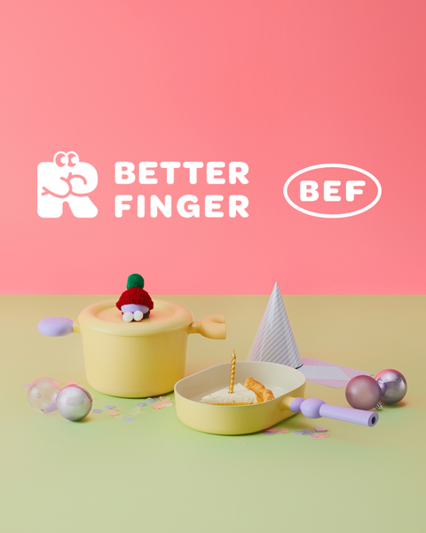 A whimsical product advertisement featuring a central figure, which is a playful representation of a finger with a red Santa hat, sitting in a yellow round container. Surrounding the figure are geometric shapes including a white pyramid and silver spheres, all placed against a two-toned backdrop with a green bottom and pink top. The text 'BETTER FINGER' in white font alongside the acronym 'BEF' in a white oval shape is displayed prominently at the top.