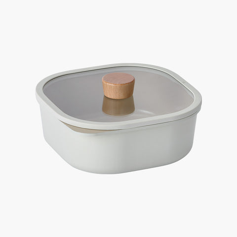 A shallow, square storage container with a glass lid featuring a wooden handle, in a neutral color.