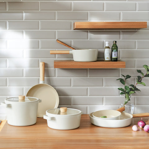 Fika collectiAlt text: "A modern kitchen setup featuring a white subway tile backsplash with two wooden shelves holding various cooking utensils and white pots. On a wooden countertop, there are additional white cooking pots and pans, along with a small plant and some onions and garlic.on photos