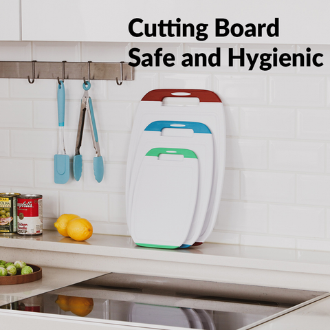 Kitchen scene with the headline 'Cutting Board Safe and Hygienic' displayed above a modern, white kitchen sink area. Two cutting boards with integrated handles in white and teal hang on the wall, beside hanging kitchen utensils with blue handles. On the counter, there are fresh ingredients, including lemons and avocados, suggesting the use of the cutting boards in food preparation.