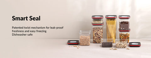 Promotional image for Smart Seal food storage solutions, showcasing a line of clear glass jars with various dry foods. The jars feature a patented twist mechanism lid, as indicated by the accompanying text, which boasts leak-proof freshness and suitability for easy freezing and dishwasher use. The containers are filled with a variety of items such as beans, pasta, lentils, and mixed spices, neatly arranged on a light beige surface against a similarly colored backdrop.