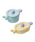 A set of two pastel-colored cookware items, including a light green pot with a lid and a yellow oval pot with a lid, both with purple handles, displayed on a white background